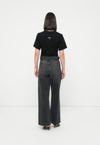 Svart kortermet T-skjorte med hvit "DAY" trykk på ryggen, sammen med høy midje, vid bukse i grå denim. Hæler synlige.