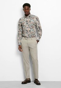 Long-sleeve shirt with a floral pattern in earthy tones, paired with light-colored trousers and dark leather shoes, creating a smart-casual look.