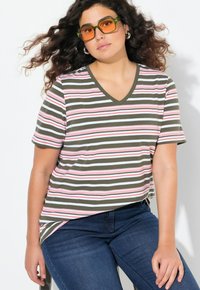 Pruhované tričko s výstřihem do V v olivové, bílé a růžové barvě. Krátké rukávy, volný střih. Kombinované s tmavě modrými džíny a oranžovými slunečními brýlemi.