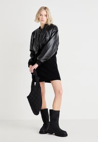 Black leather cropped bomber jacket, fitted black skirt, tall black boots, and a quilted black tote bag. Simple design with sleek textures.