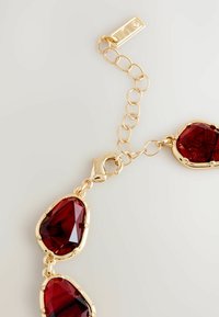 Złoty naszyjnik z łańcuszka z dużymi, szlifowanymi, głęboko czerwonymi kamieniami w nieregularnych kształtach oraz zapięciem typu lobster.