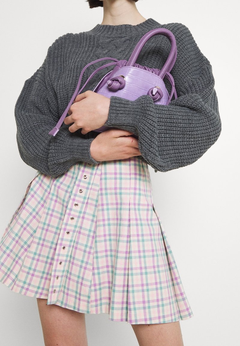 Pull en maille épaisse gris avec un col haut, associé à une jupe à carreaux pastel avec des boutons. Un petit sac à main lavande avec une surface texturée.