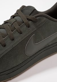 Zelené semišové tenisky se sladěnými tkaničkami, s šedým znakem Nike, texturovanou gumovou podrážkou a polstrovaným límcem pro pohodlí.