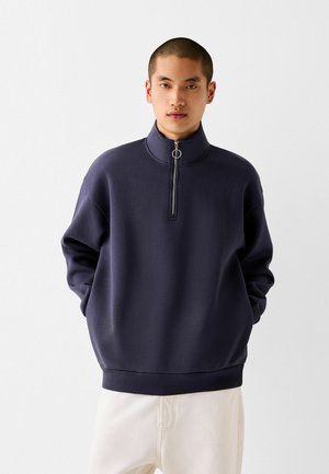 Marineblå pullover sweatshirt med høj krave og kvart længde lynlås. Lavet af blødt materiale, med ribbede manchetter og kant, afslappet pasform.