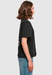 Svart bomull T-skjorte med korte ermer og en avslappet passform, med hvite grafiske design på forsiden. Kombinert med blå denimjeans.