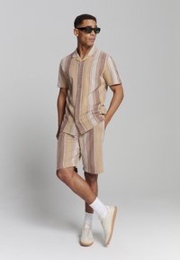 Korte mouwen blouse met knopen en bijpassende shorts in beige en bruine strepen, gemaakt van lichte stof. Gekocht met een zonnebril en sneakers.