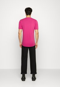 T-shirt fucsia a maniche corte in una vestibilità rilassata, realizzata in morbido cotone, abbinata a pantaloni neri e stivali alla caviglia. Texture liscia, design minimal.
