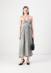Abito lungo di colore grigio chiaro con corpino arricciato, spalline regolabili e un accento arancione. Abbinato a scarpe col tacco nere e una borsa nera.