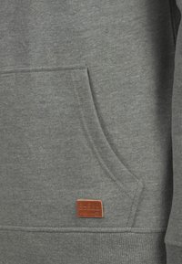 Grå sweatshirt med en frontlomme, ribbede manchetter og kant. Har et lille brunt lædermærke med "BLEND" præget. Blødt bomuldsblandingsstof.