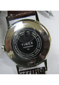 Montre Timex avec fond en acier inoxydable, modèle TW2W93300. Elle est dotée d'un bracelet en cuir marron et de détails gravés, y compris les informations sur la résistance à l'eau.