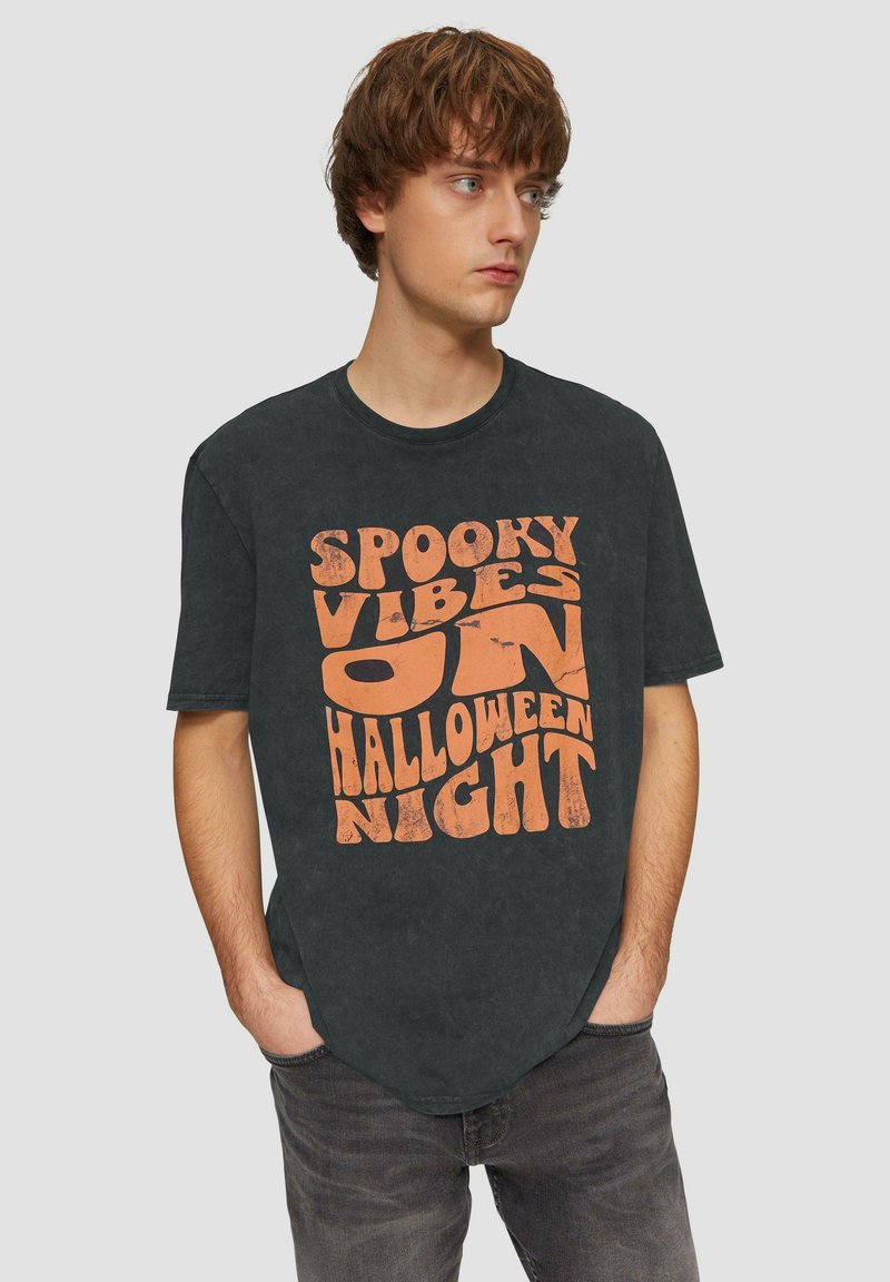 Zwarte katoenen t-shirt met een ronde halslijn en korte mouwen, met de tekst "SPOOKY VIBES ON HALLOWEEN NIGHT" in versleten oranje lettertypen.