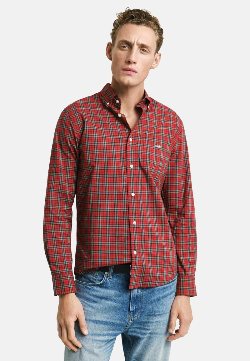 Camisa de cuadros rojos de manga larga con botones blancos, con un cuello abotonado y un pequeño logo en el pecho. Combinada con jeans azules.