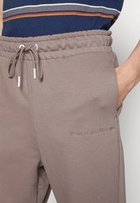 Ljusbruna joggingbyxor med elastisk midja och dragsko. Har sidoficka och broderad text: "det är inte på dig, det är inom dig."