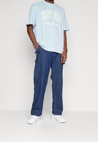 Camiseta de algodón de color azul claro con el logo "TOMMY JEANS NEW YORK" en blanco, combinada con jeans de mezclilla de color azul oscuro y zapatillas blancas.