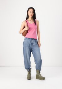 Top sin mangas de color rosa, jeans de mezclilla sueltos de color azul claro y botas hasta el tobillo de color verde oliva. Bolsa marrón con correa para el hombro.