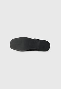Black boot sole with textured grip pattern and a small embossed brand name on plain light background.