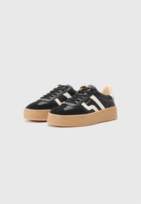 Svart sneakers med en kombinasjon av semsket skinn og lær, hvite striper og en lys brunt gummisåle. Designet med runde snøringer og polstret krage.