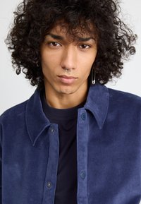 Navy corduroy shirt with a button-down collar, front snap closure, and soft texture, layered over a black, round-neck t-shirt.