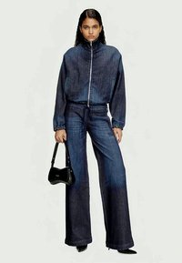 Chaqueta de denim con cremallera en la parte delantera, con un cuello alto y puños elásticos, combinada con pantalones de denim de pierna ancha. Acento de bolso negro.
