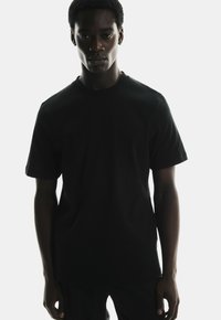 Black crew-neck t-shirt displaying a smooth cotton texture with short sleeves, featuring a fitted silhouette and minimal seams for a sleek design.