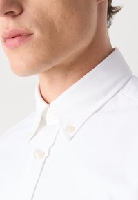 Witte button-up shirt met een gestructureerde kraag, gemaakt van een gladde stof. Beschikt over twee knopen nabij de kraag voor het vastmaken.