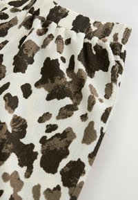 Buks med elastisk talje i blødt stof, der har en lys cremet baggrund med et uregelmæssigt brun og mørkebrun cow-print mønster.