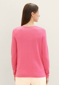 Pull rose à manches longues avec un col rond, texture douce et poignets côtelés. Design simple, sans motifs ni logos visibles.