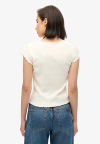 Hvid ribbet t-shirt med korte, bølgede ærmer og en bølget halsudskæring, parret med højttaljede blå denimjeans.