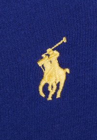 Modrá tkanina s vyšívaným logem žlutého polo hráče, které se vyznačuje složitým stehem a hladkou texturou.