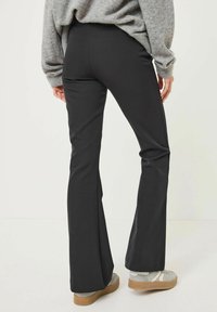 Pantalons évasés noirs en tissu extensible, avec une texture lisse et une taille ajustée, associés à un pull en laine grise et des chaussures de couleur claire.