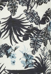 Květinová tkanina s tmavě modrými tropickými listy a světle modrými květy na bílém pozadí, s texturovaným vzhledem.