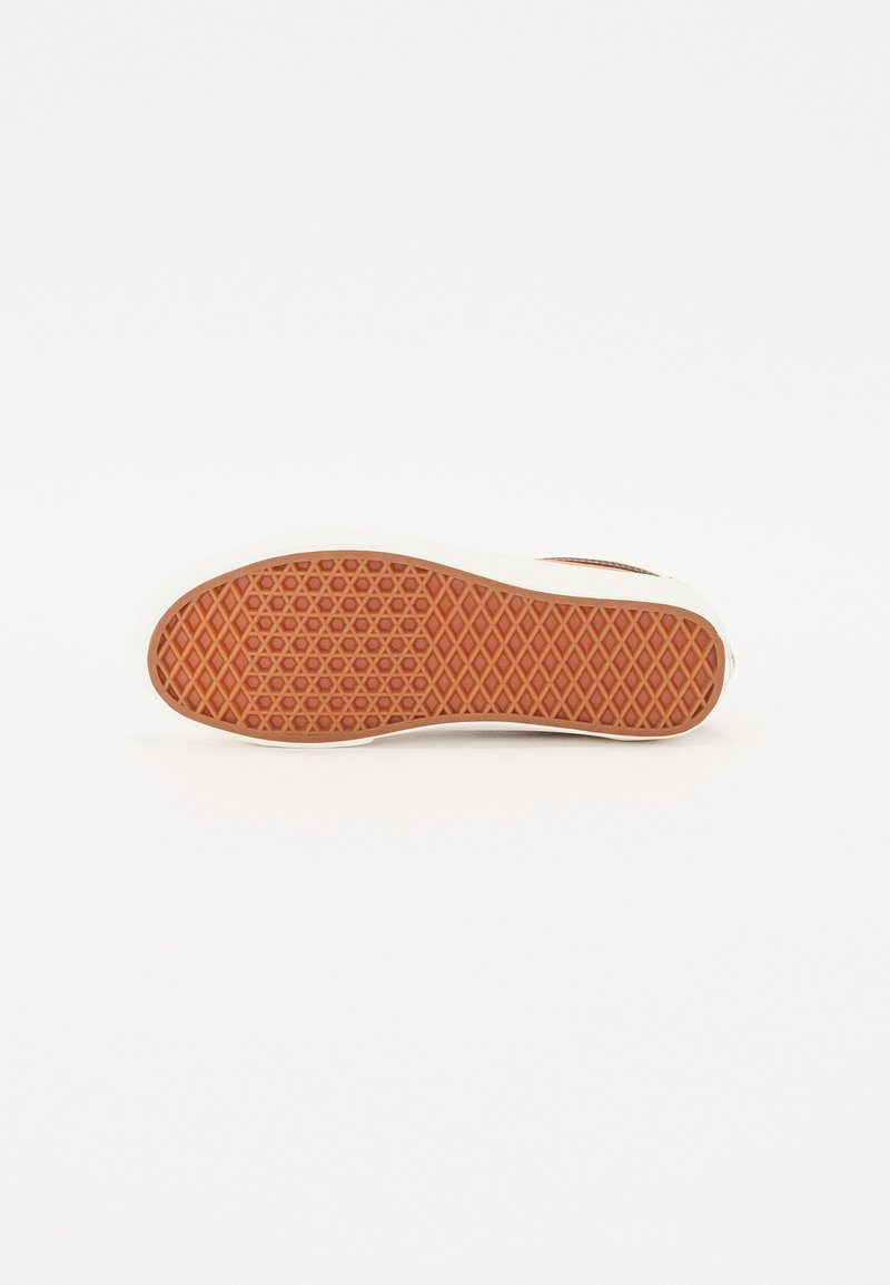 Semelle d'une chaussure avec une surface en caoutchouc texturé orange présentant un motif en losanges, entourée d'une semelle intermédiaire blanche.