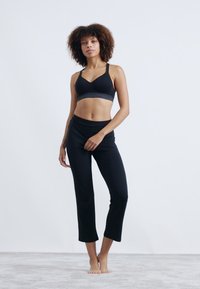 Soutien-gorge de sport noir avec une bande grise, accompagné de leggings courts noirs. Tissu lisse, design ajusté, adapté pour les vêtements de sport.