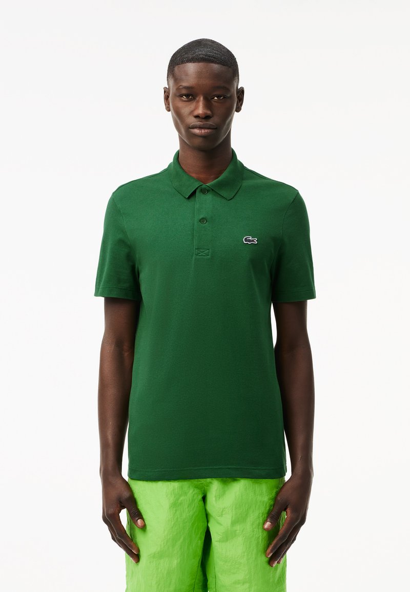 Camisa polo verde de algodón texturizado con tapeta de tres botones y logotipo bordado, combinada con pantalones cortos de color verde brillante.