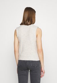 Bezramenný pletený top ve světle béžové barvě s ribbovanou strukturou, s neořezanými okraji. V kombinaci s tmavě šedými džíny s vysokým pasem.