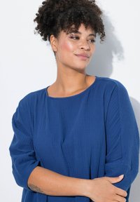 Maglietta blu con texture, collo rotondo e maniche a tre quarti, caratterizzata da una vestibilità rilassata e un tessuto morbido. Senza motivi o accenti visibili.