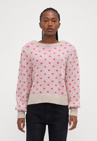 Lys beige sweater med pinke prikker, bred rund hals og ribbede manchetter og kant. Strikket struktur med en afslappet pasform.
