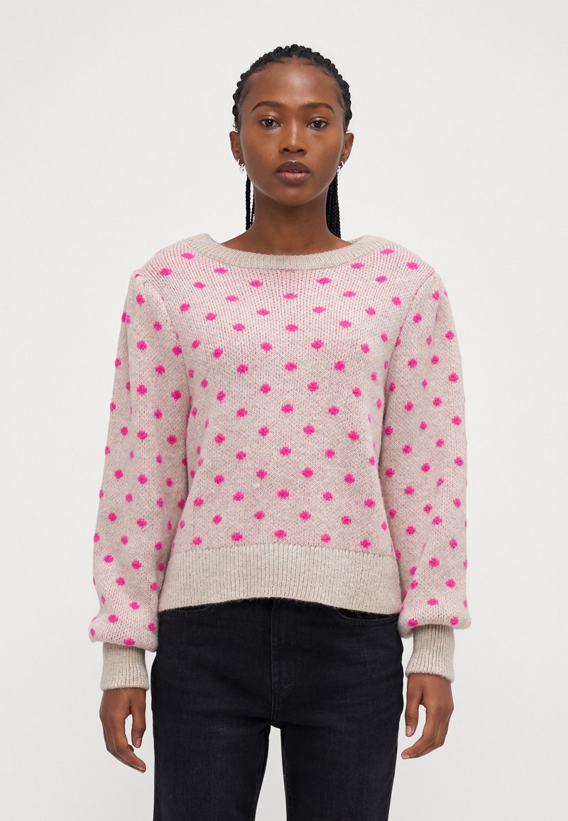 Lys beige sweater med pinke prikker, bred rund hals og ribbede manchetter og kant. Strikket struktur med en afslappet pasform.