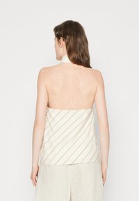 Top bez ramínek z off-white tkaniny s diagonálními hnědými pruhy. Hladký povrch, halter neck design a volný střih.