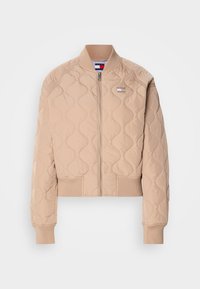 Veste bomber matelassée beige avec col, poignets et bas en côte, fermeture éclair devant, et petit patch logo Tommy Hilfiger sur la poitrine.