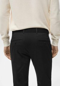 Pantaloni neri con una vestibilità slim, dotati di due tasche posteriori e dettagli in bottone discreti, abbinati a un maglione texturizzato beige chiaro.