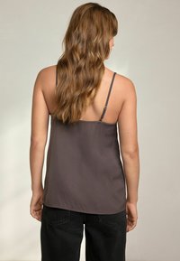 Top marrone con spalline sottili, texture liscia, vestibilità ampia e orlo dritto, abbinato a jeans neri a vita alta.