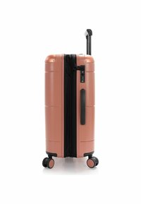 Hard-shell suitcase in rose gold with a black zipper and handle. Features four wheels, integrated combination lock, and smooth texture.