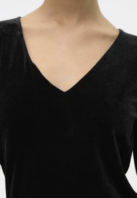 Haut en velours noir avec un décolleté en V profond et une texture douce, soulignant une apparence lisse et luxueuse sans embellissements ni motifs.