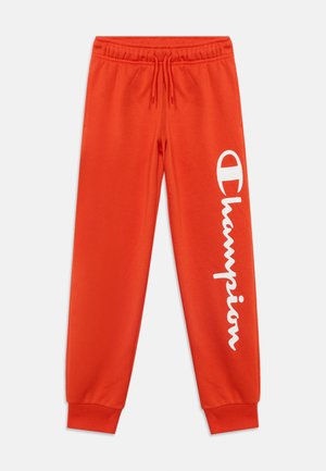 Pantalon de survêtement orange vif avec taille et poignets élastiques, avec un grand logo blanc "Champion" sur la jambe gauche.