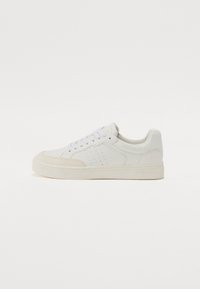 White leather sneaker with a low profile, round toe, perforated accents, flat laces, and a rubber sole. Minimalistic design with beige details.