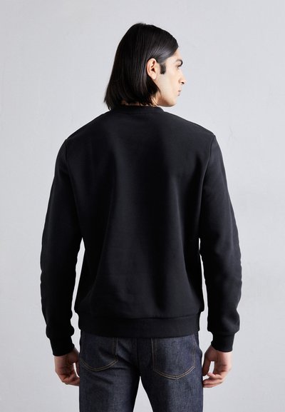 Sort, langærmet sweatshirt med rund hals, der har en glat overflade og ribbede detaljer ved håndleddene. Båret med mørke denimjeans.