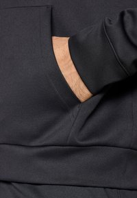 Μαύρο, μαλακό φούτερ με κουκούλα και μπροστινή τσέπη, με ραμμένα μανίκια και λεία υφή. Διαθέτει ά νετη εφαρμογή και μινιμαλιστικό σχέδιο.