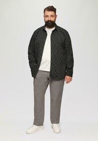 Zwarte knoopshirt met witte stippen, gedragen over een wit T-shirt. Grijze broek en witte sneakers maken de outfit compleet.