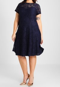 Navy blue lace dress with a fitted bodice, short sleeves, and a flared skirt. Features a scalloped neckline and intricate lace pattern.